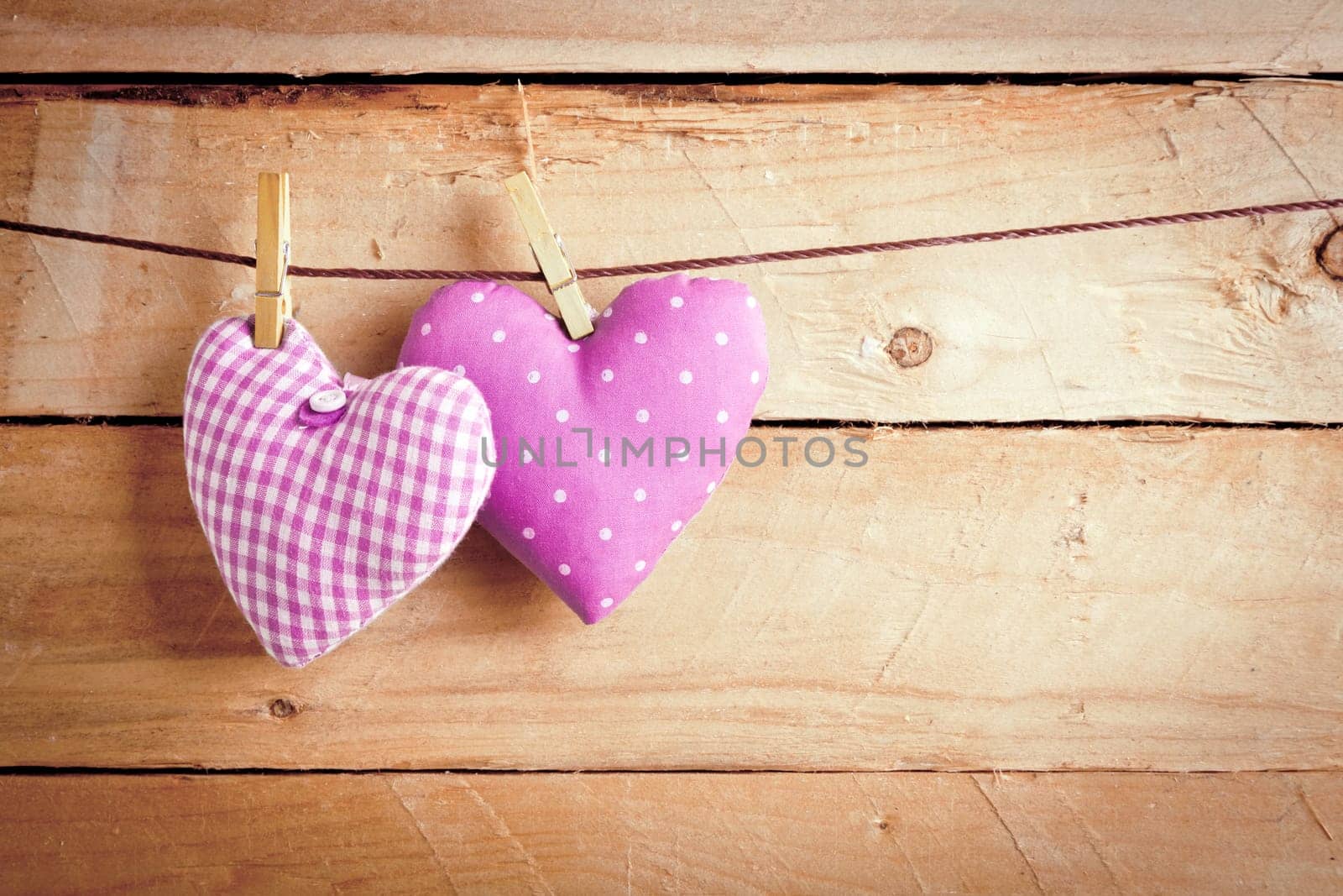 Two pretty pink material Valentine hearts hanging on a line with clothes pags over wooden boards.