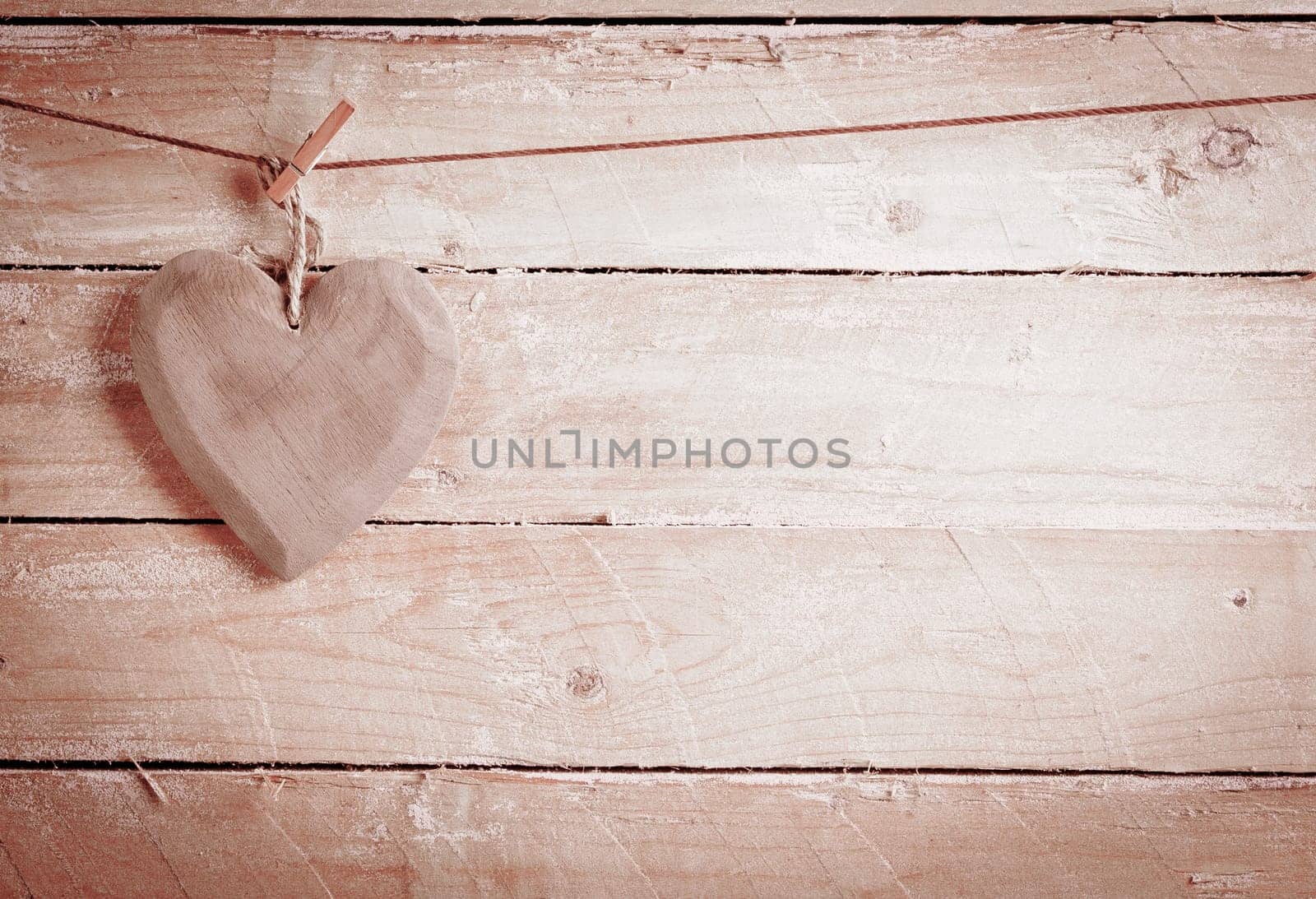 Quaint rustic wooden heart hanging from a peg against wooden boards with copyspace in a concept of love and romance