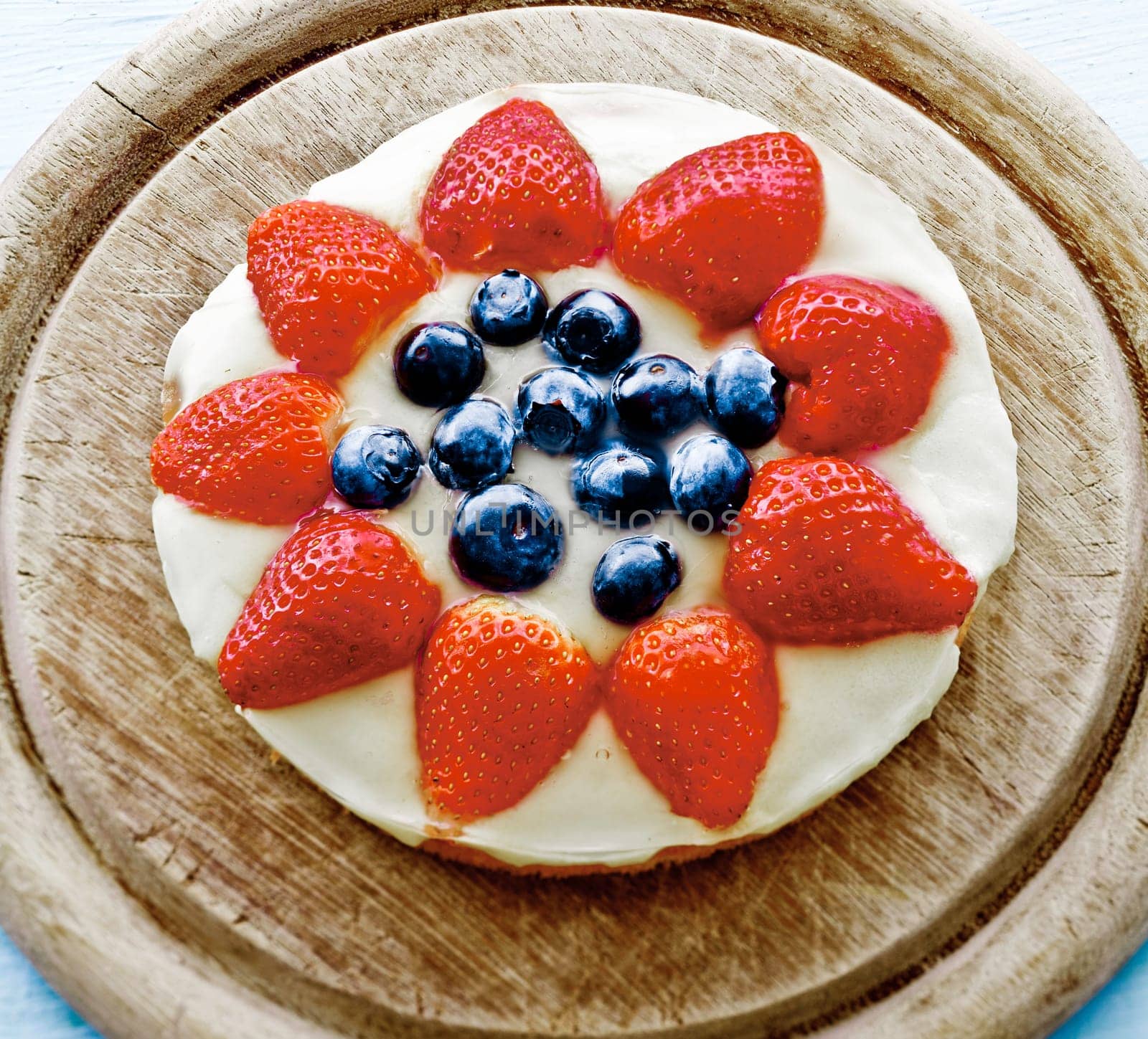 Rich Gourmet strawberry tarte of a striped cake base topped with chocolate and blueberries on a wooden plate