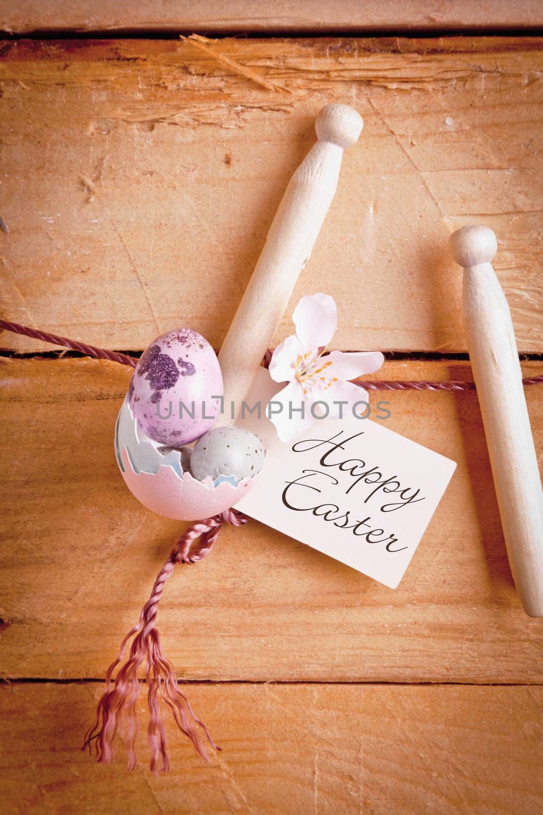 Label with handwritten Happy Easter hanging from rustic wooden pegs with Ester Eggs on a backdrop of wooden boards.