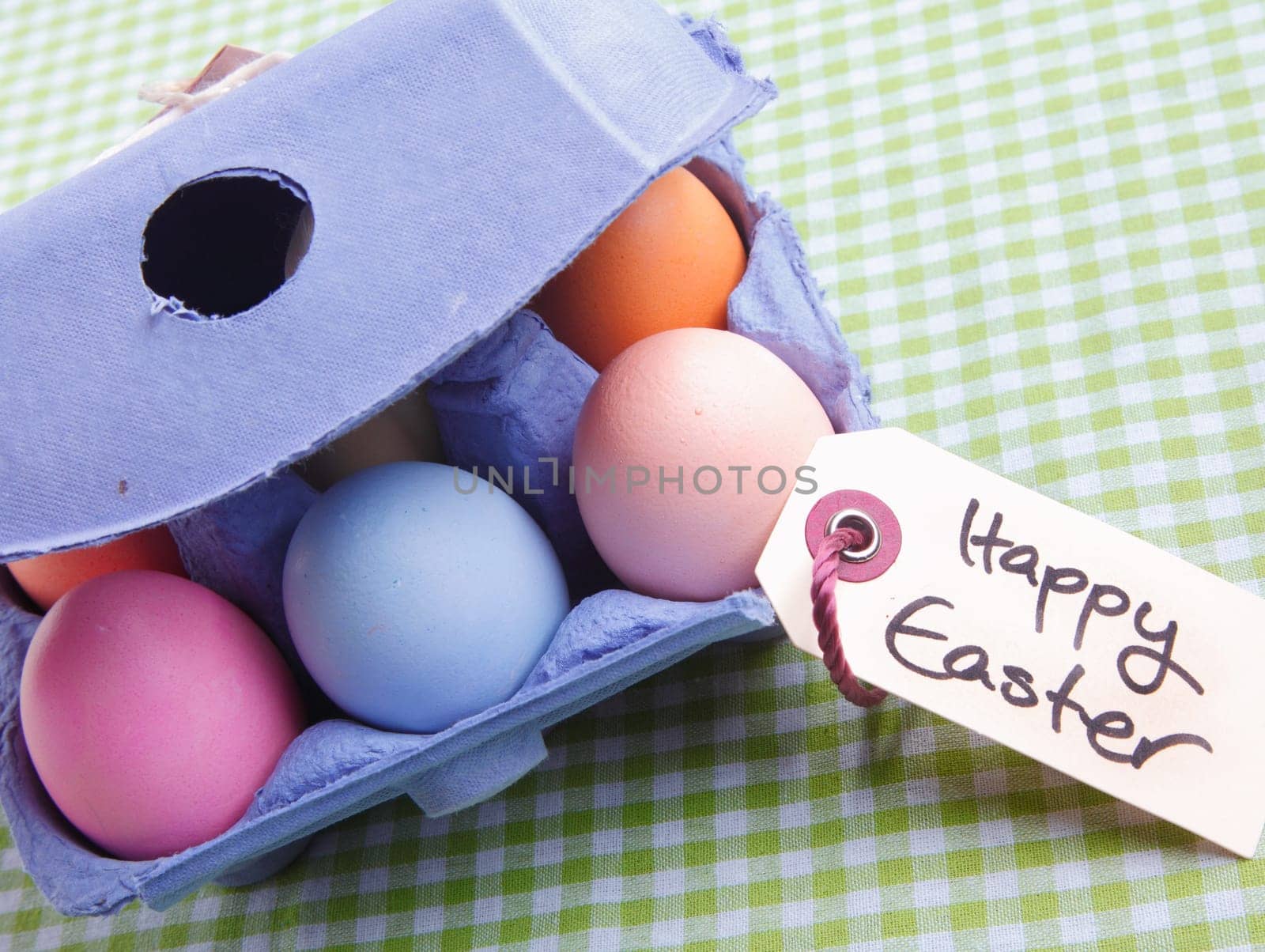 Egg carton with different colored Eggs. On a green checked background with a handwritten memo Happy Easter