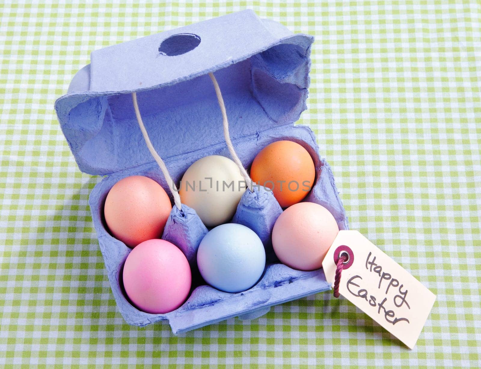 Egg carton with different colored Eggs. On a green checked background with a handwritten memo Happy Easter