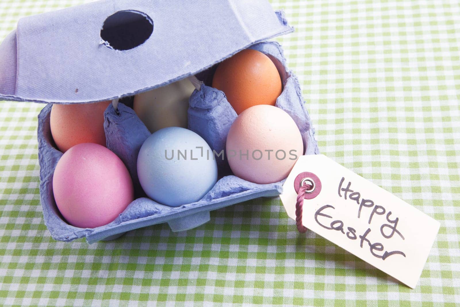 Egg carton with different colored Eggs. On a green checked background with a handwritten memo Happy Easter