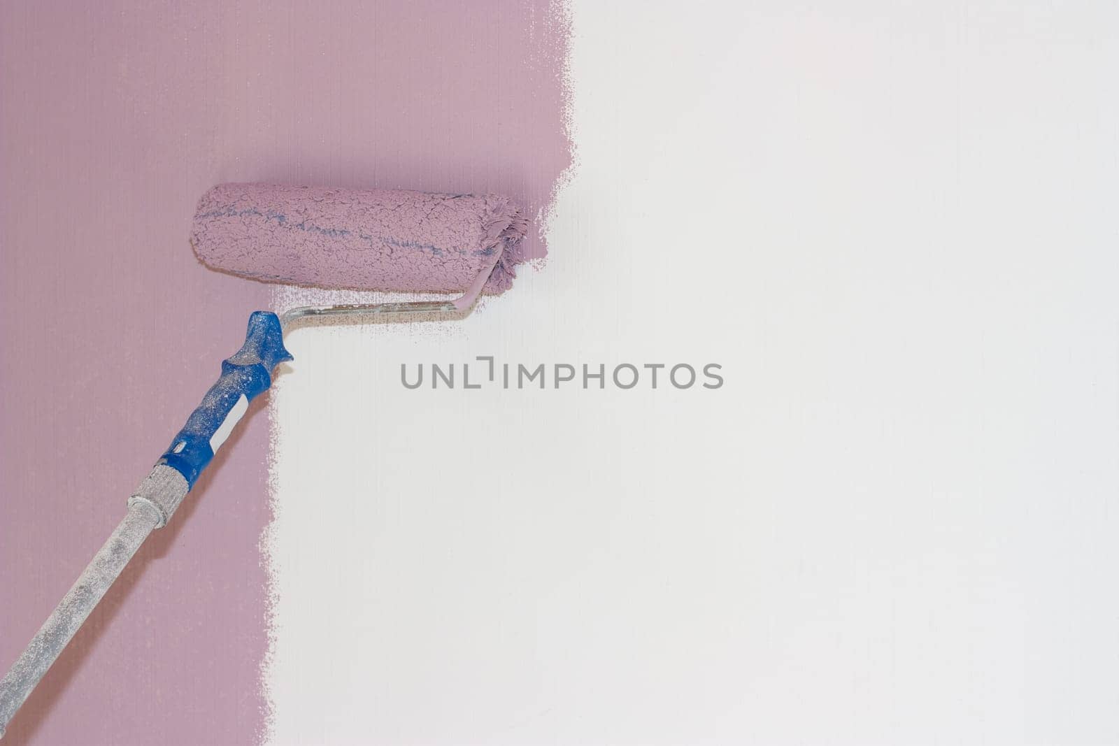 A roller with a pink color on the white wall.