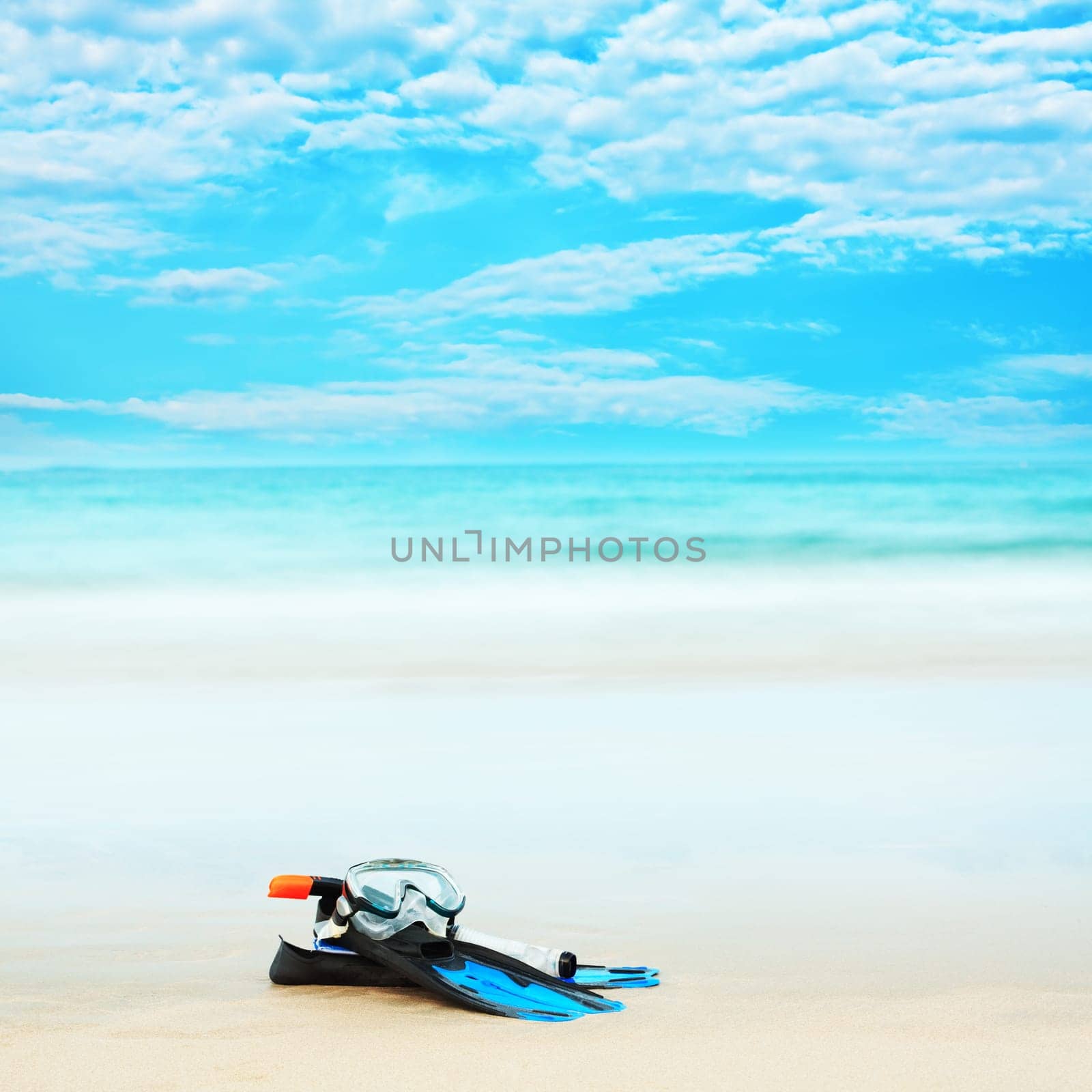 Snorkeling equipment mask and fins on white sand beach.