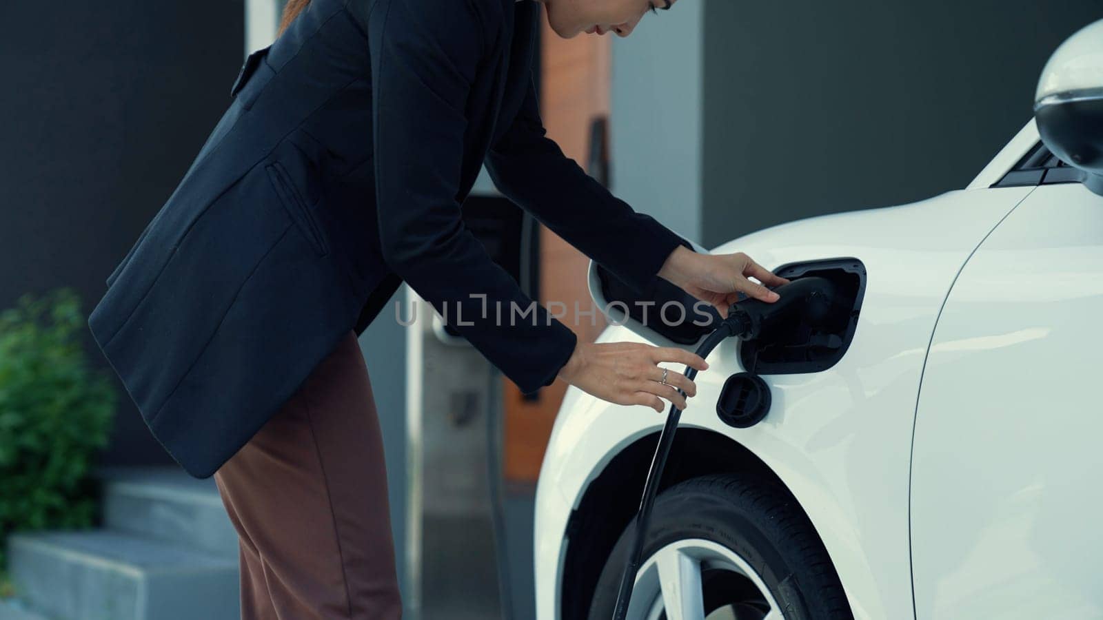 Progressive woman installs a charging station plug into her electric vehicle at home. EV automobiles provide an environmentally beneficial concept of clean and green energy.