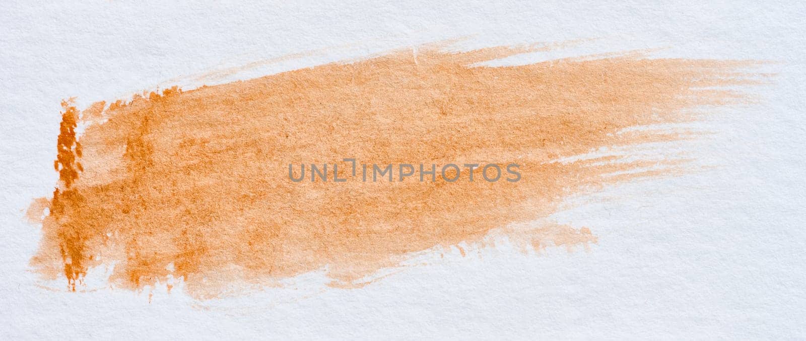 A stroke of orange watercolor paint on a white sheet of paper