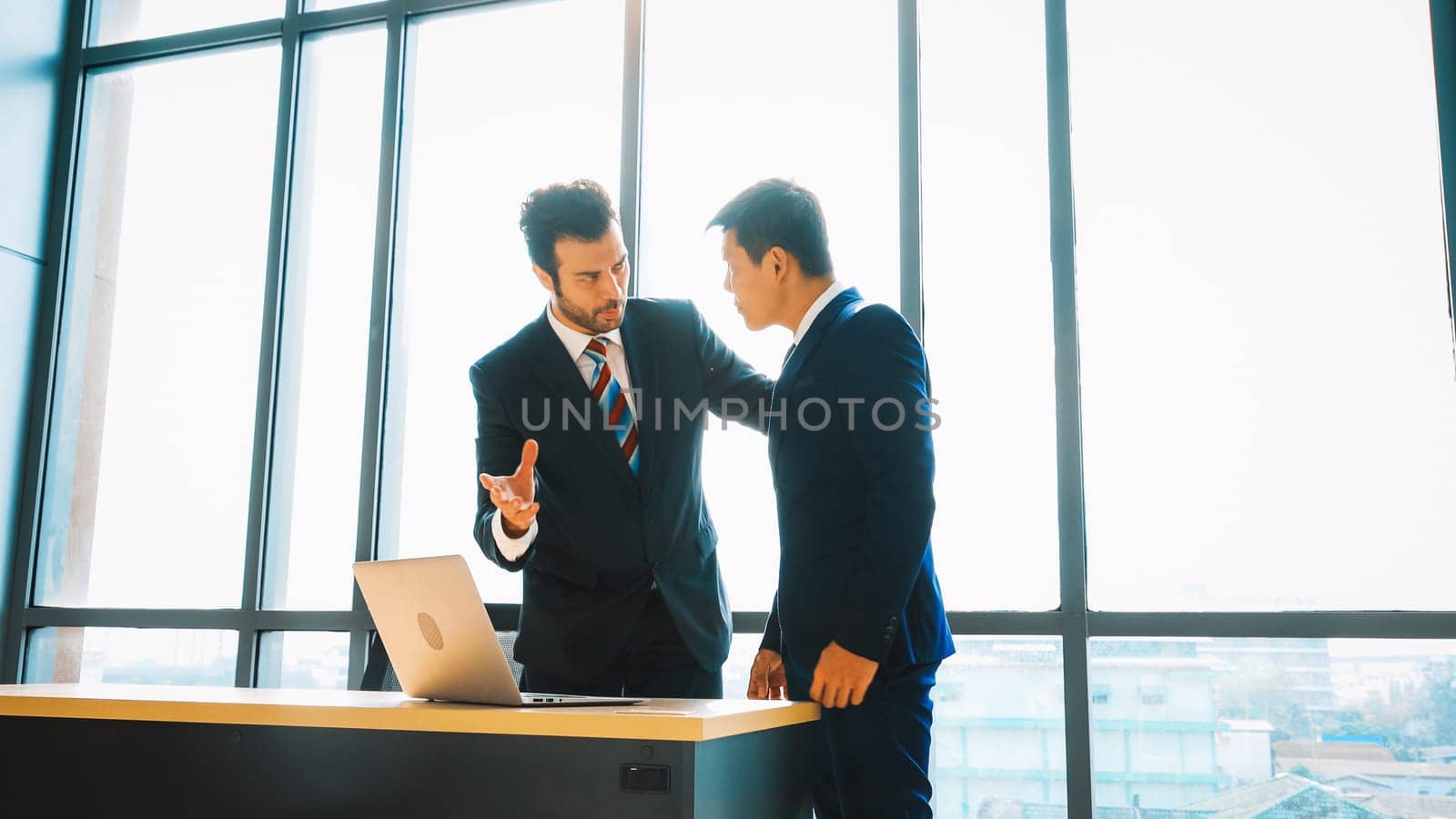 Two business people talk project strategy at office meeting room. Businessman discuss project planning with colleague at modern workplace while having conversation and advice on financial report. Jivy