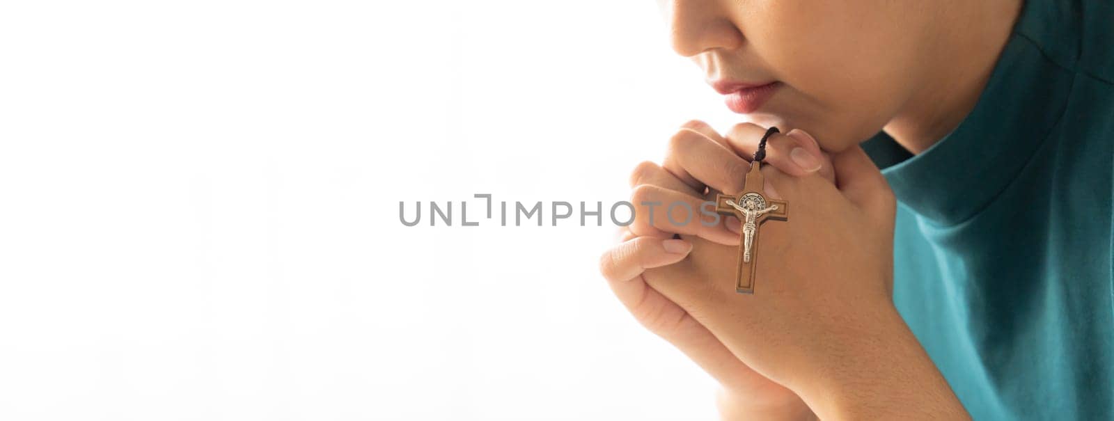 Praying female hand holding cross while praying to god faithfully. Concept of hope, religion, faith, christianity and god blessing for happiness. Bright light, white blurring background. Burgeoning.