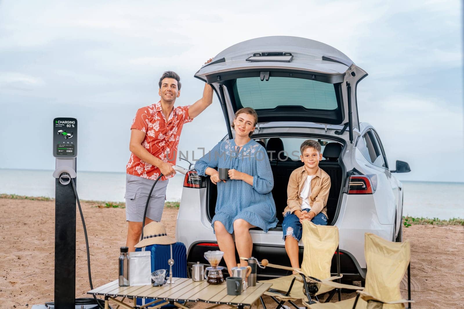 Family vacation trip traveling by the beach with electric car, happy family recharge EV car, enjoying outdoor camping coffee. Seascape travel and eco-friendly car for clean environment. Perpetual