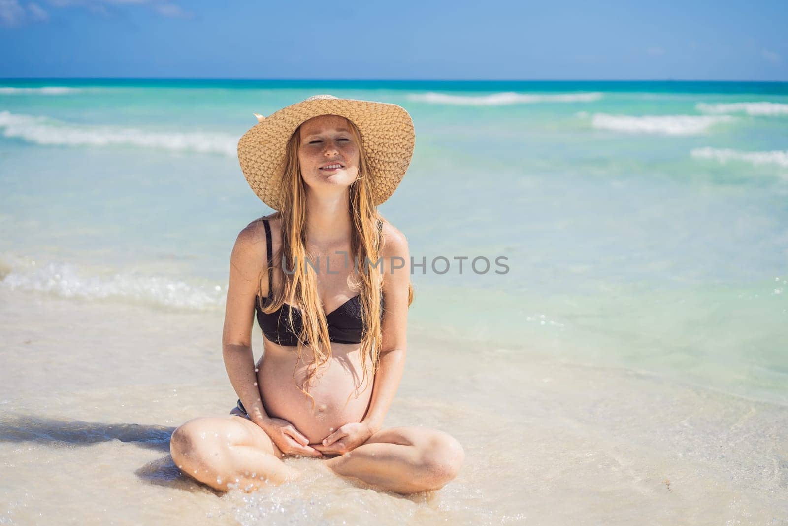 Radiant and expecting, a pregnant woman stands on a pristine snow-white tropical beach, celebrating the miracle of life against a backdrop of natural beauty.