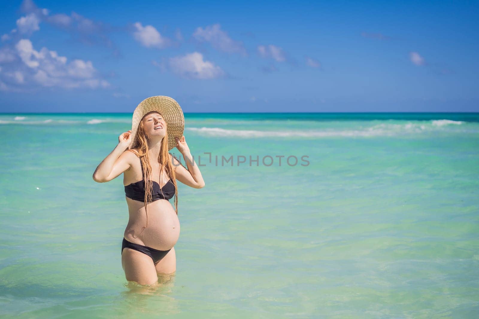 Radiant and expecting, a pregnant woman stands on a pristine snow-white tropical beach, celebrating the miracle of life against a backdrop of natural beauty.