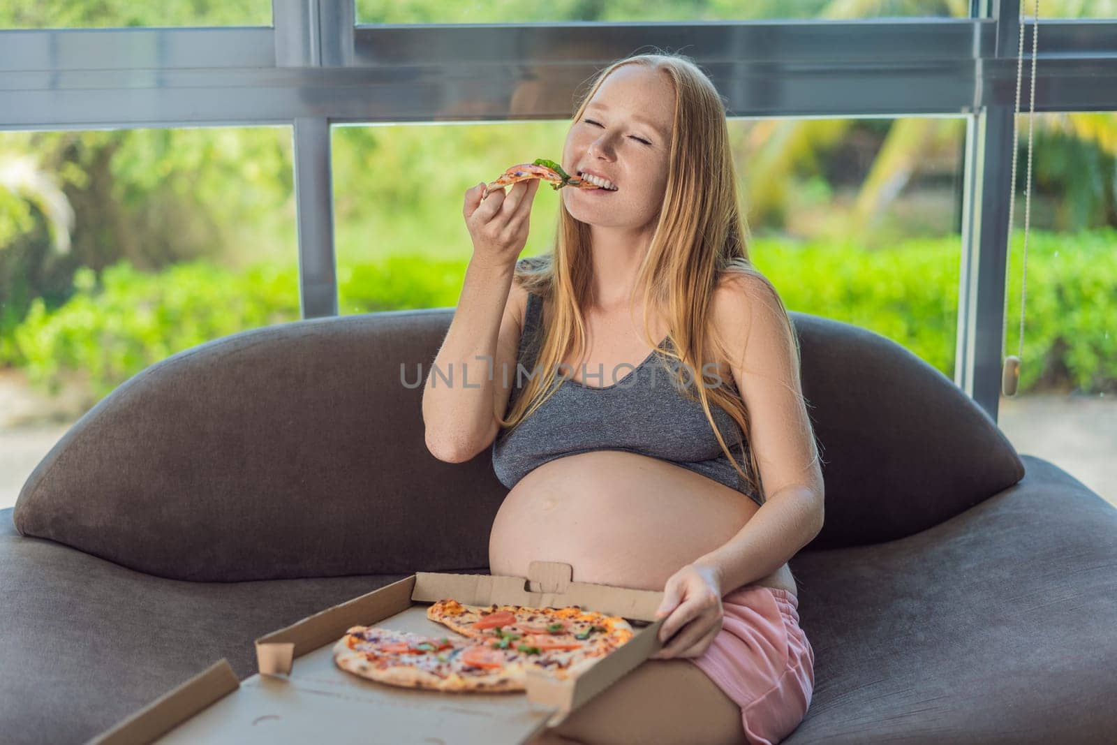 A pregnant woman enjoys a slice of pizza, savoring a moment of indulgence while satisfying her craving for a delightful, comforting treat. Excited Pregnant Young Lady Enjoying Pizza Holding Biting Tasty Slice Posing With Carton Box. Junk Food Lover Eating Italian Pizza. Unhealthy Nutrition Cheat Meal.