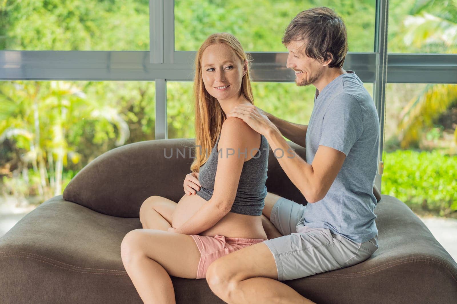 health, pregnancy and happy people concept - husband giving his wife back massage at home.