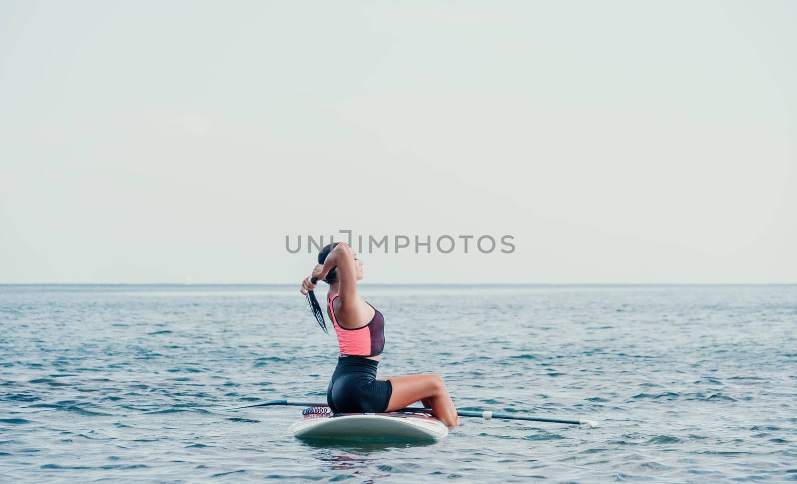 Sea woman sup. Silhouette of happy young woman in pink bikini, surfing on SUP board, confident paddling through water surface. Idyllic sunset. Active lifestyle at sea or river by panophotograph