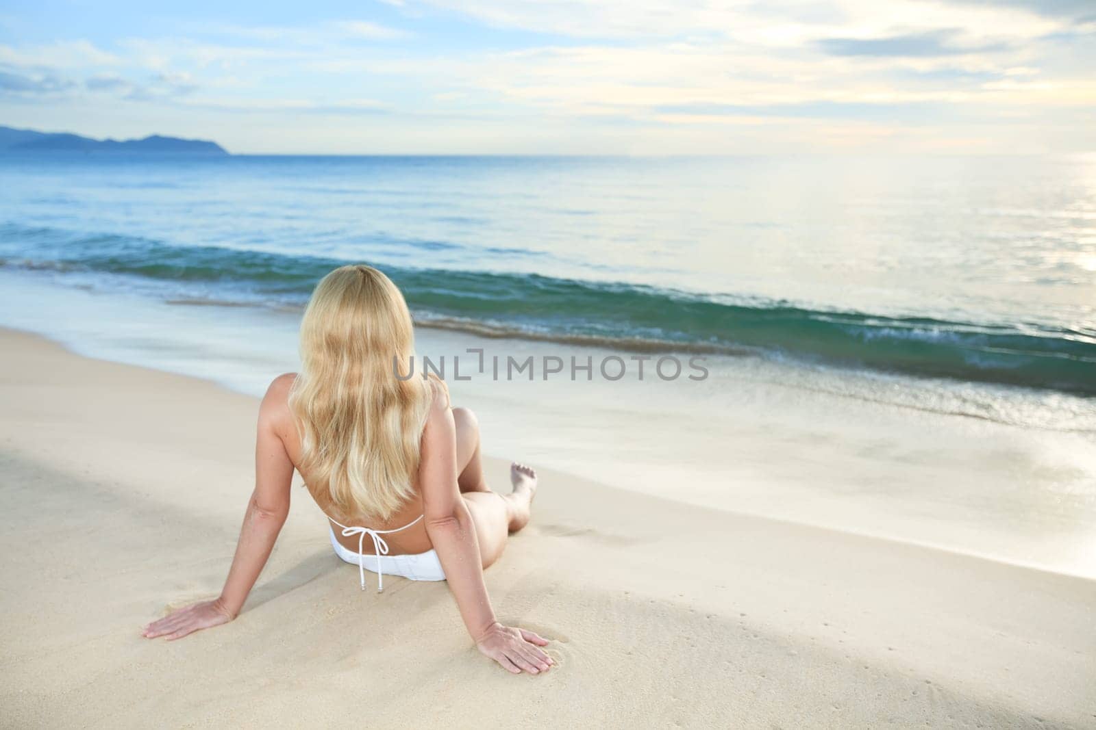 Woman sitting near the ocean at sunrise time