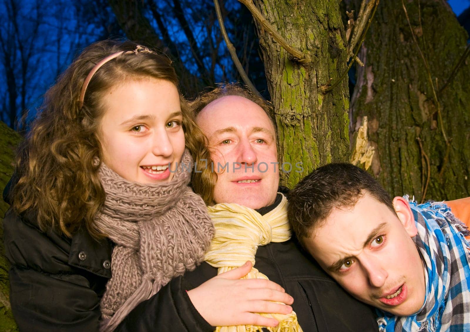 Portrait of a father with his two teenage teenagers in front of a tree at dusk