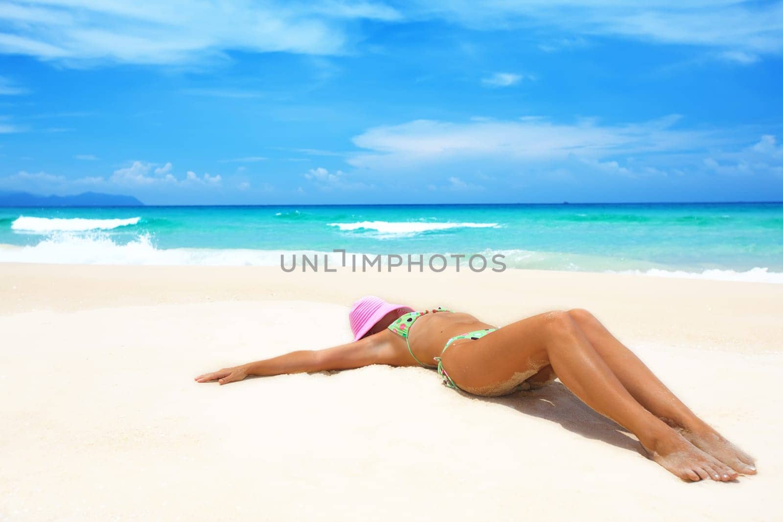 Woman in pink hat lies on the beach