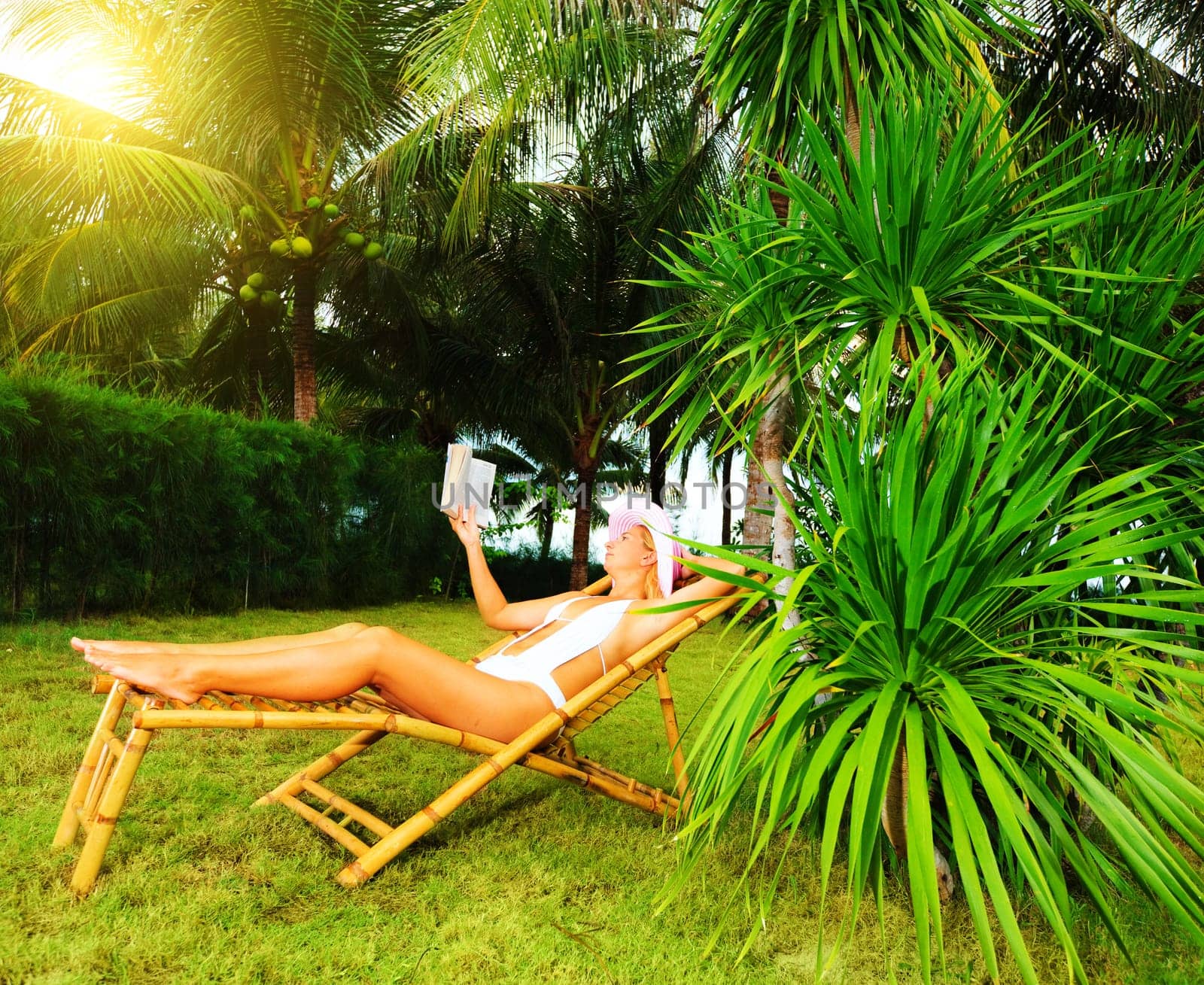 Young woman reading the book in the tropical garden