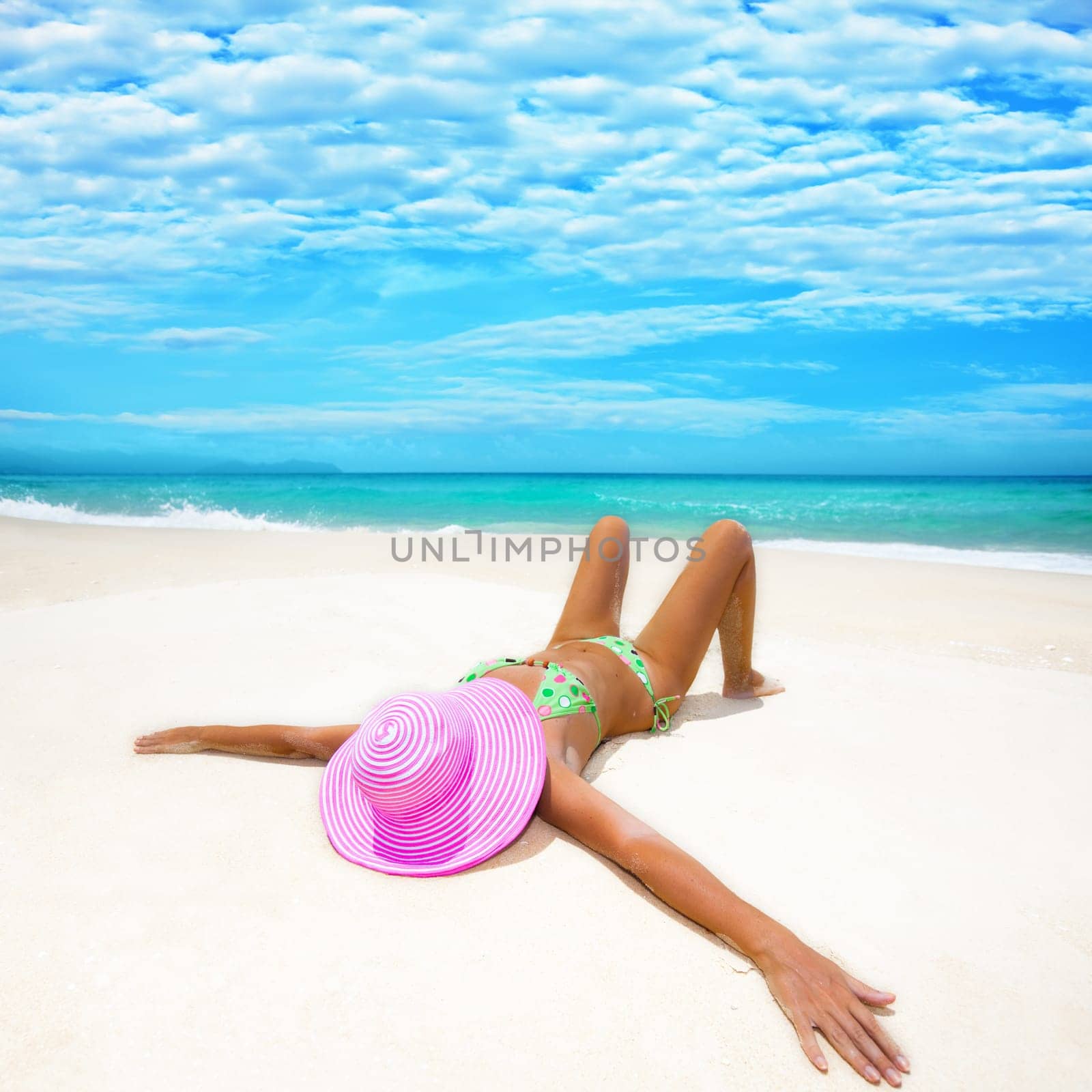 Woman in pink hat lies on the beach