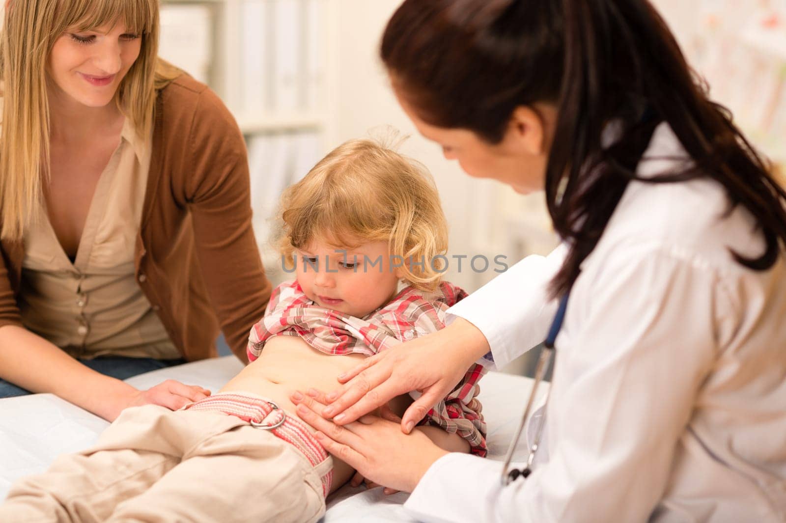 Little girl having tummy examination by pediatrician at medical office