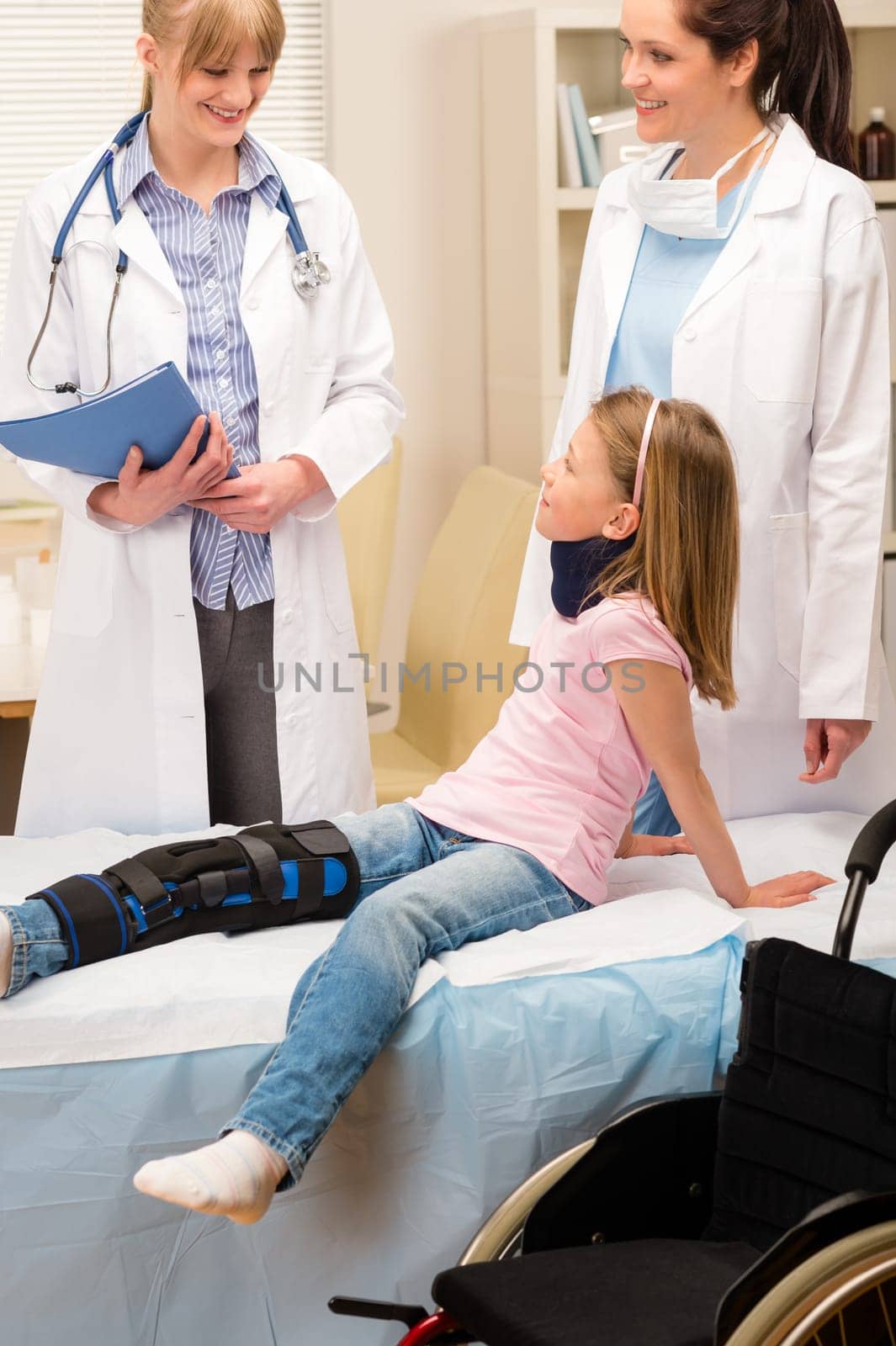 Two female doctors examine broken leg little girl wheelchair