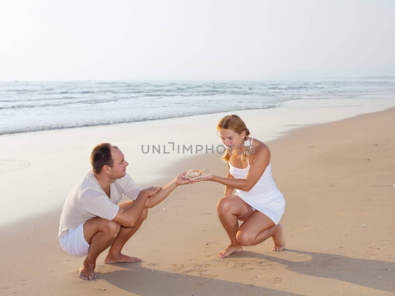 young couple with seashell on the tropical beach at sunrise time