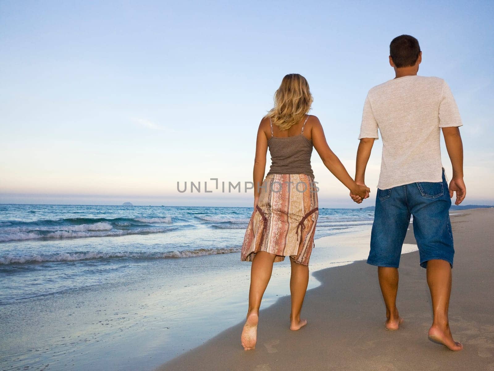 Young couple walking near the ocean on sunset time