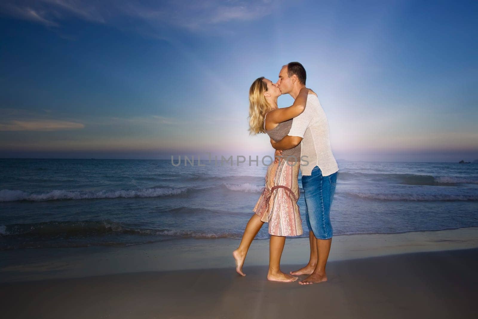 Young couple kissing near the ocean on sunset time