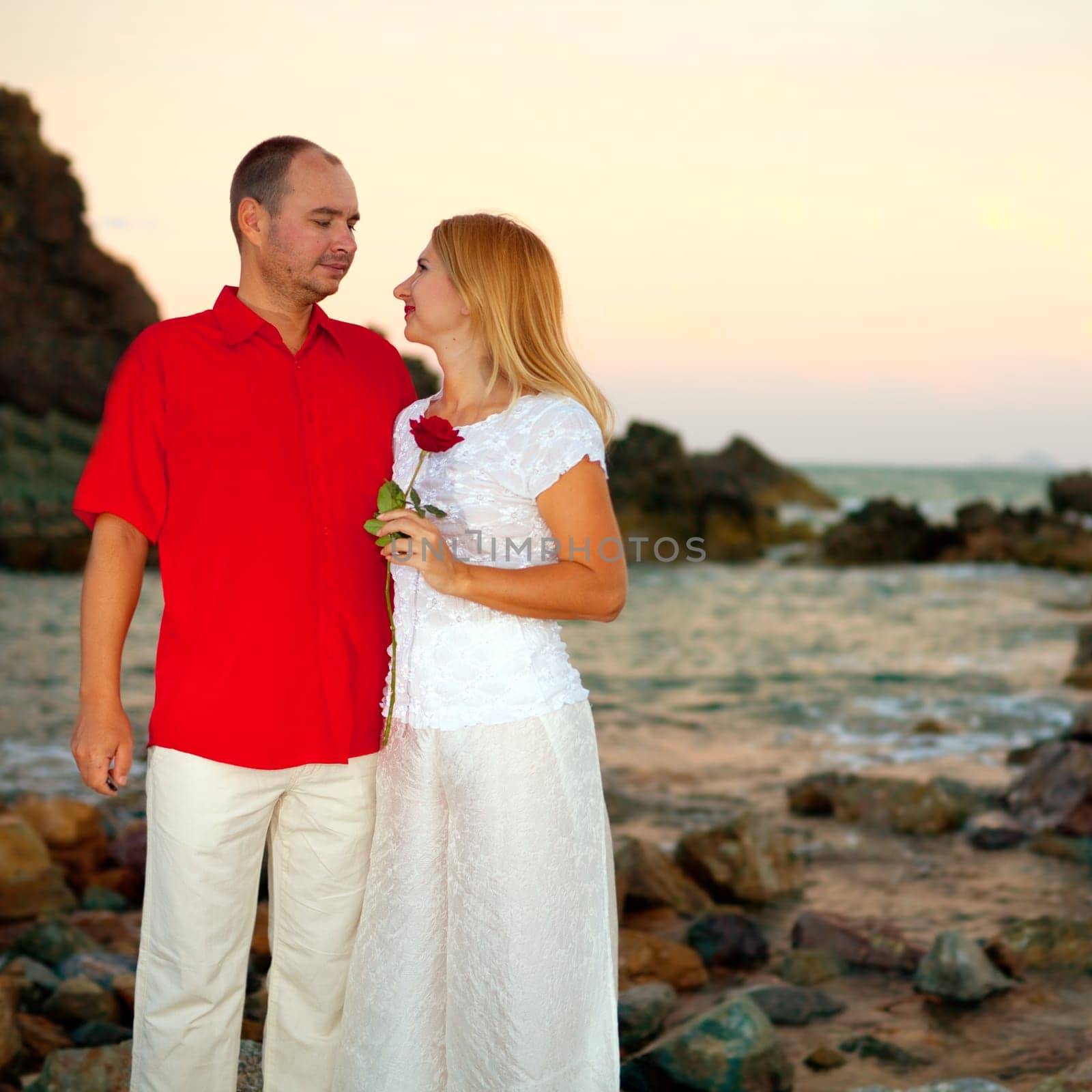 Young couple near the ocean with flowers on sunset time