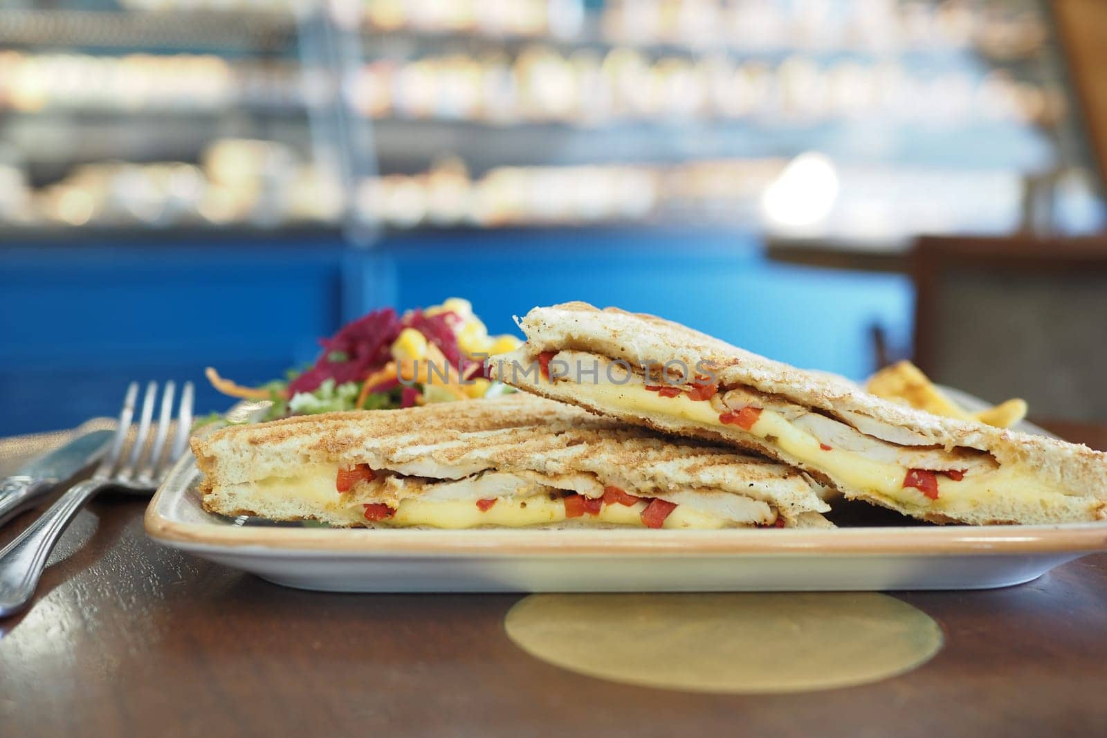 A grilled sandwich filled with cheese and chicken on a plate with salad.