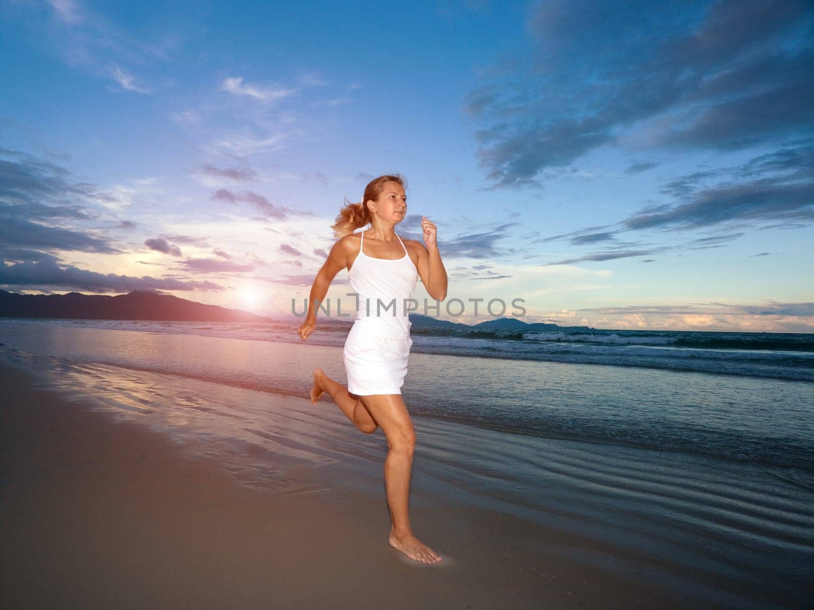 Young woman is running near the ocean at sunset time