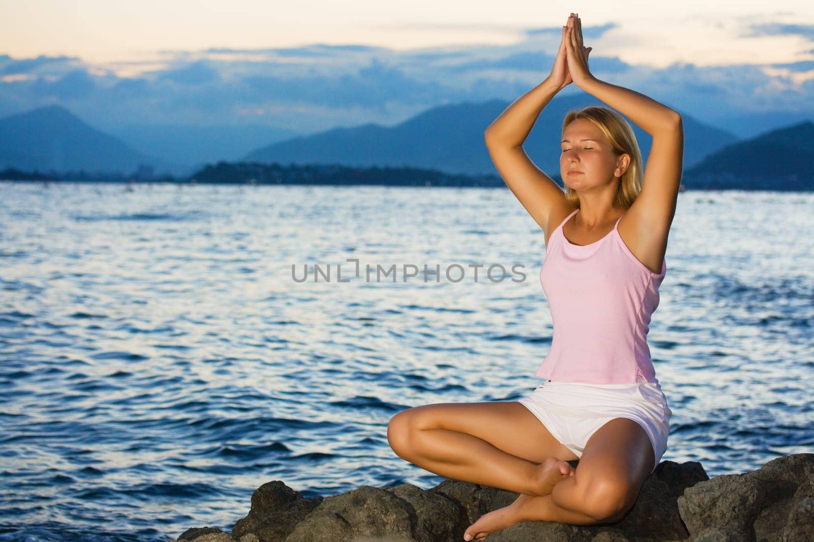 Young woman meditating at sunset time near ocean