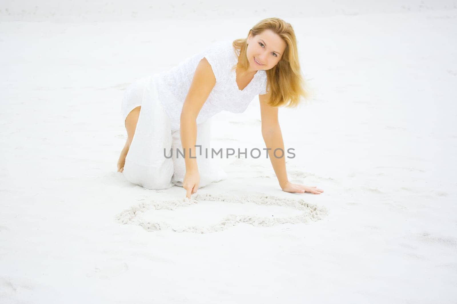 Young woman draws heart on white sand