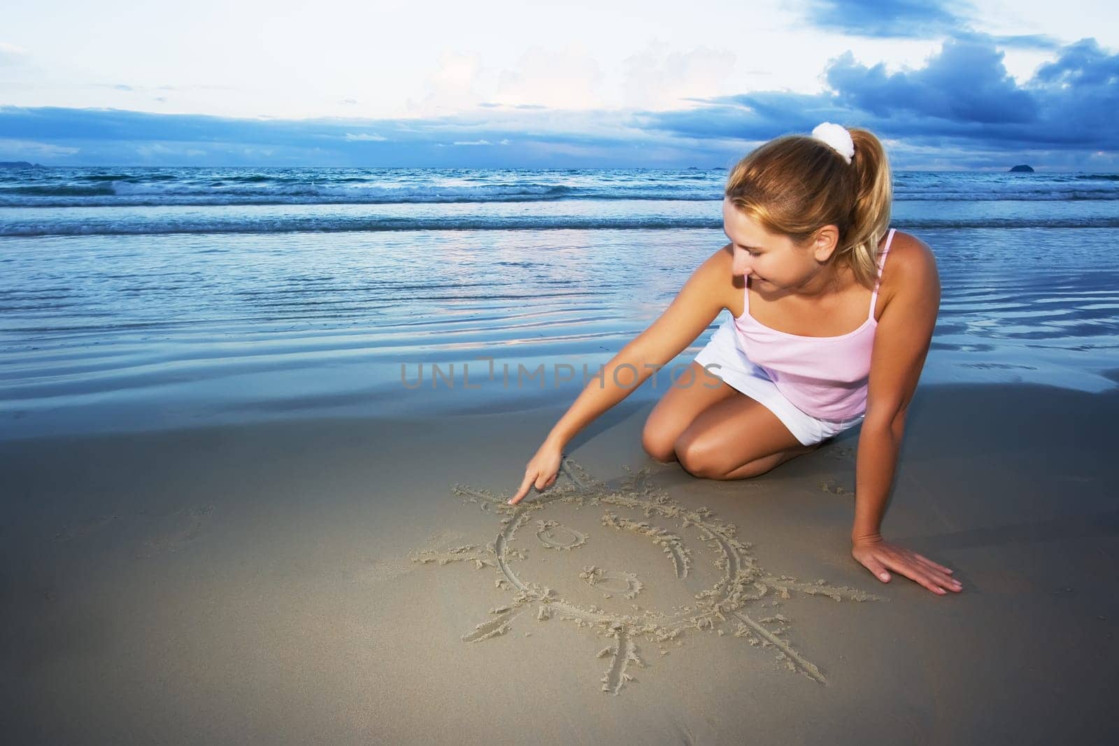 Young woman draws sun near the ocean on sunset time