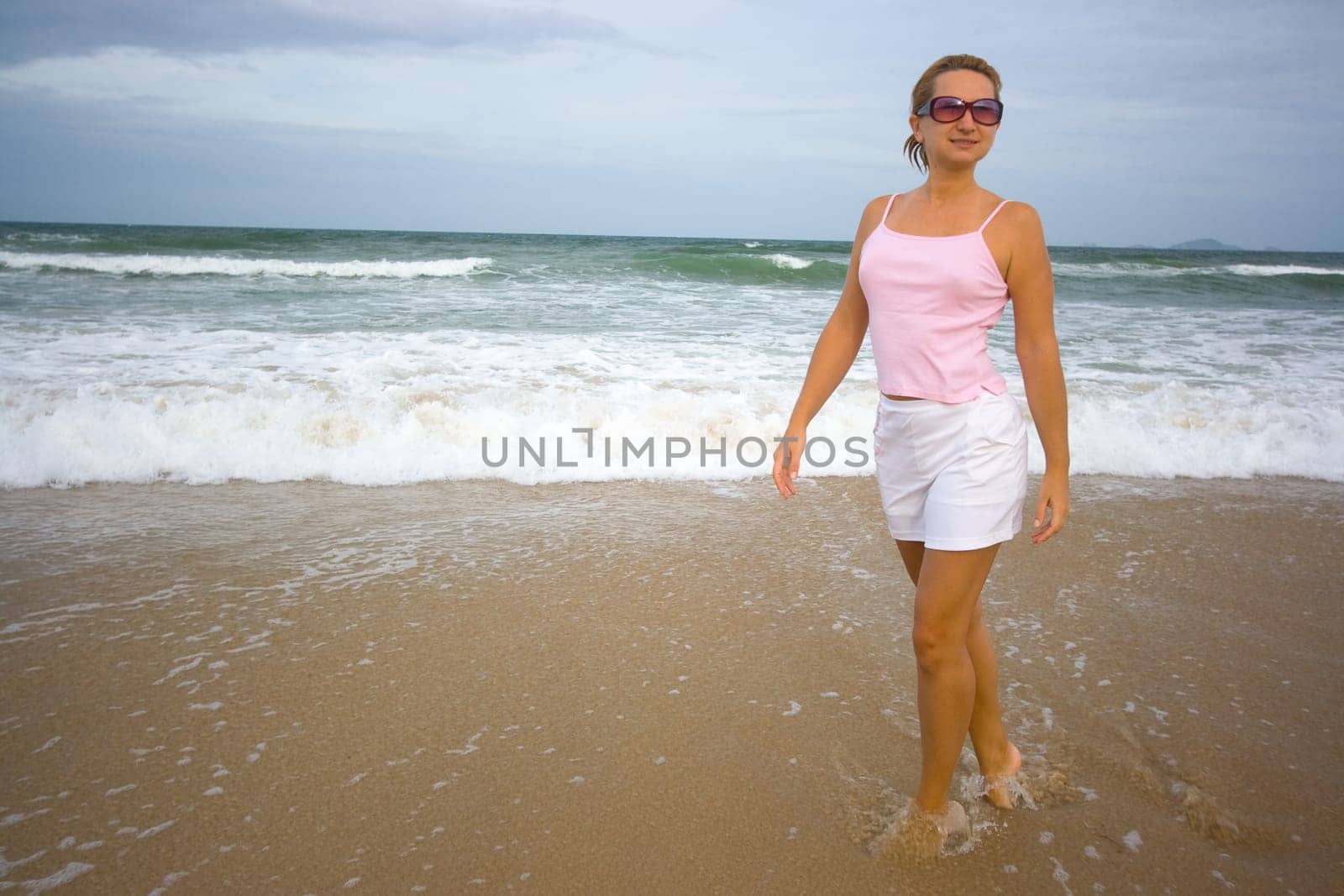 Young woman walking near ocean in sunglasses