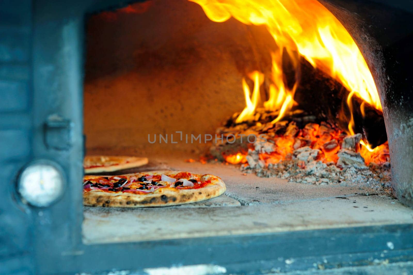 Baking Pizzas in a wood burning pizza oven with glowing coals and embers with flames shooting up