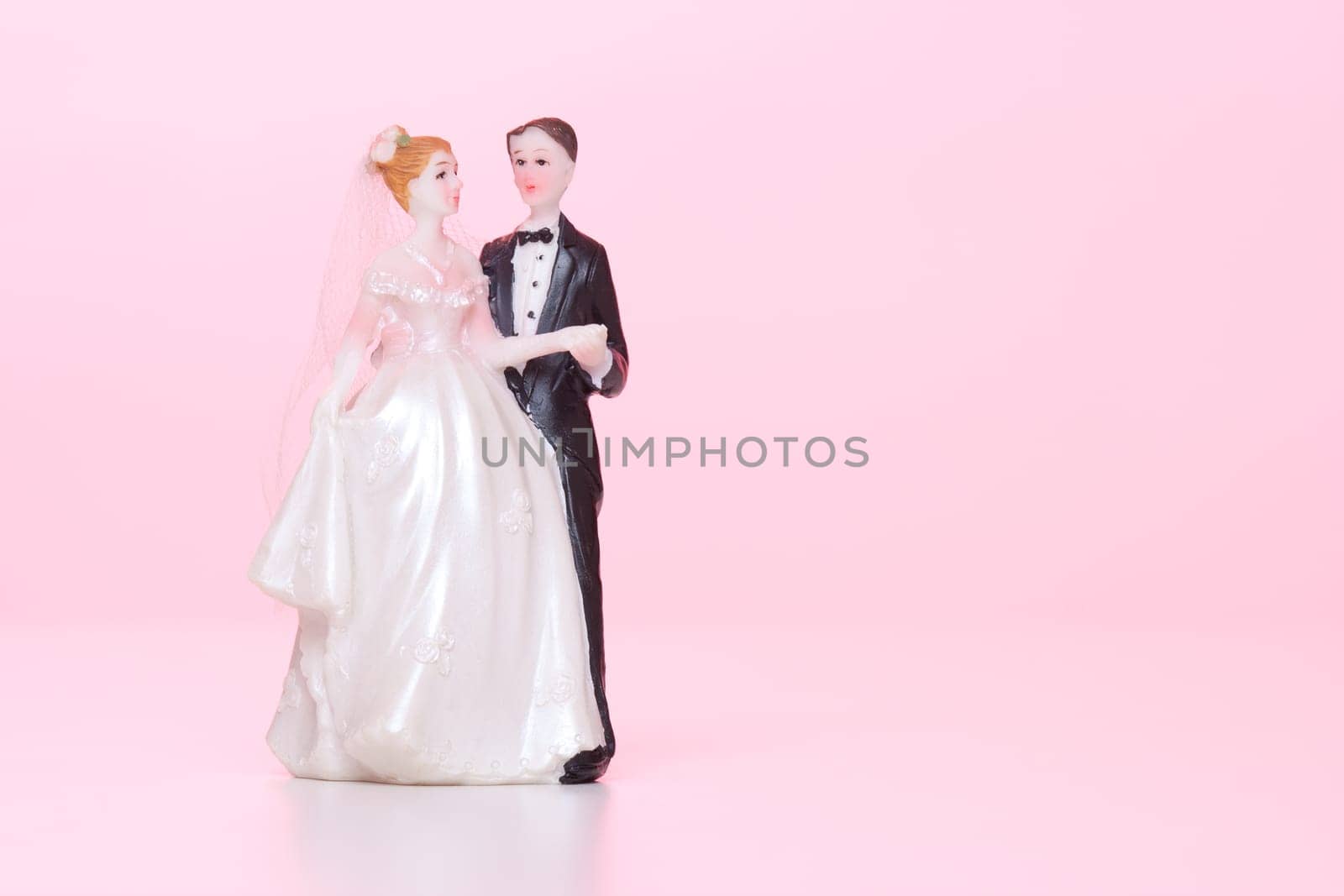 Wedding figurines (bride and groom) on pink background.