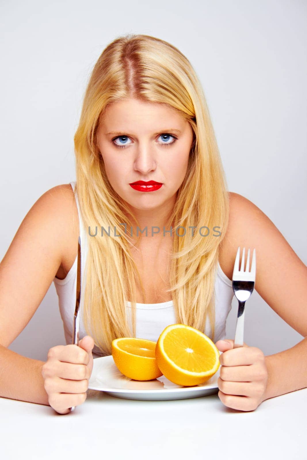 Unhappy young woman eating fruit with cutlery