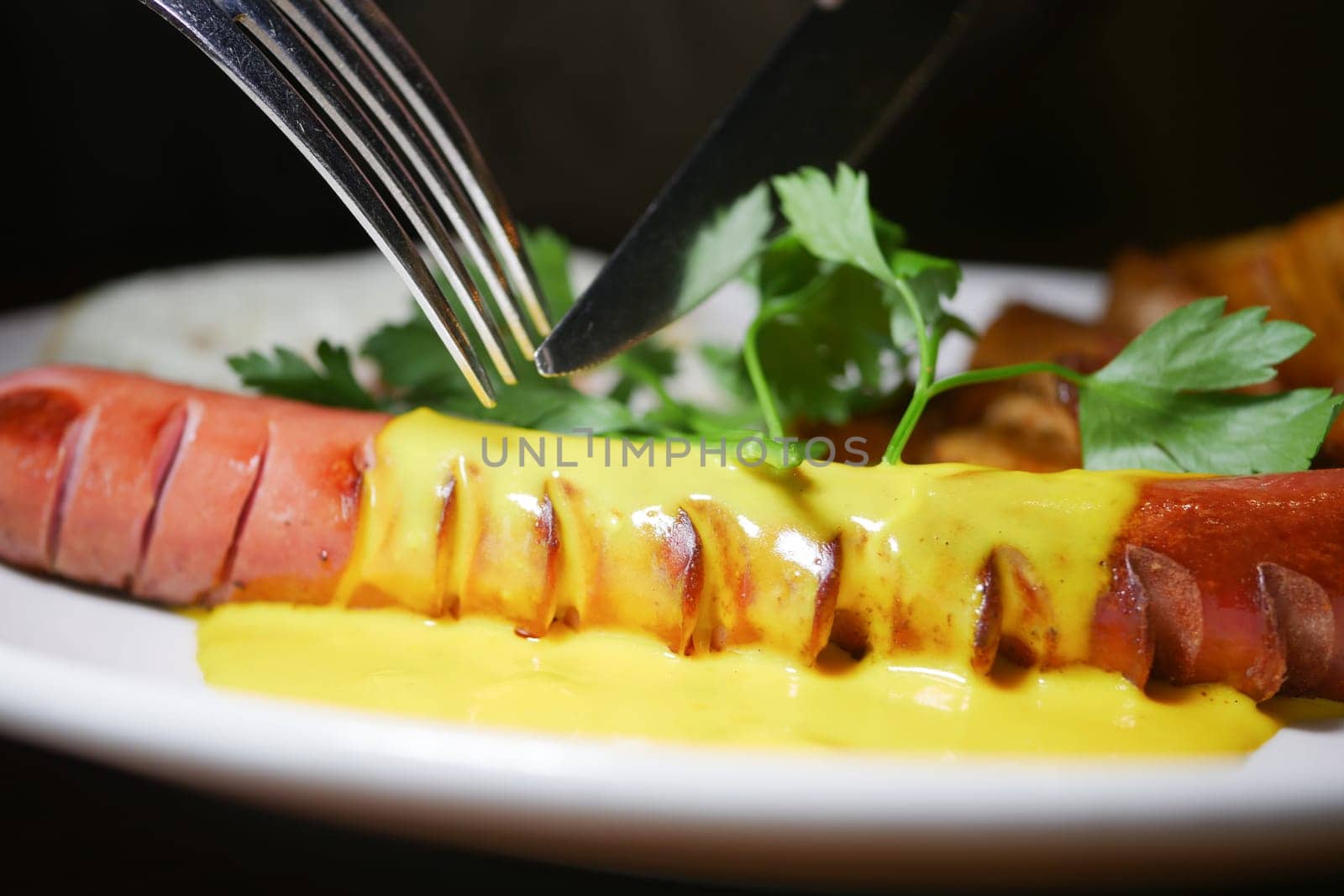 A person is preparing to eat a hot dog with mustard and garnish.