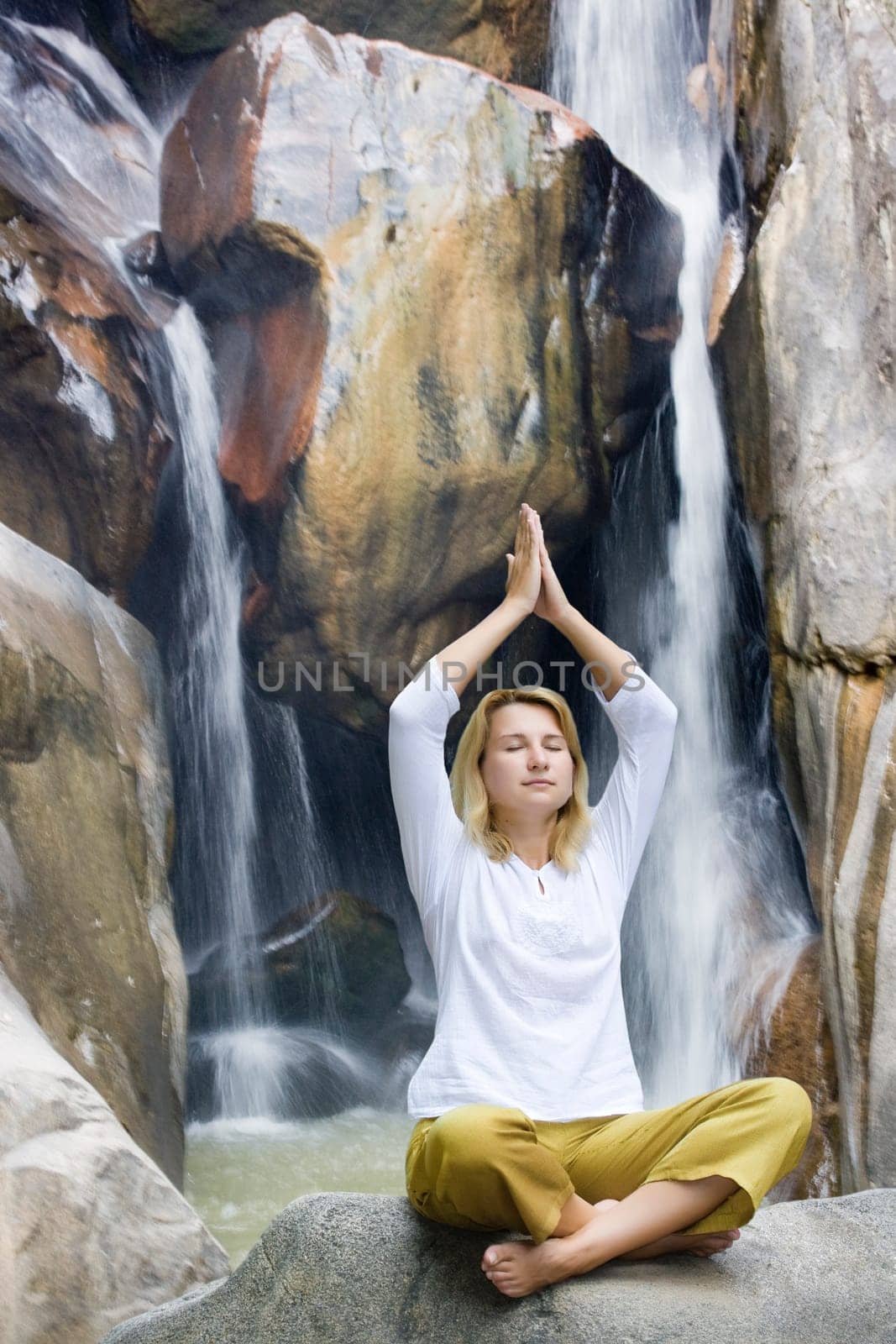 Young woman doing yoga exercises over waterfall background.
