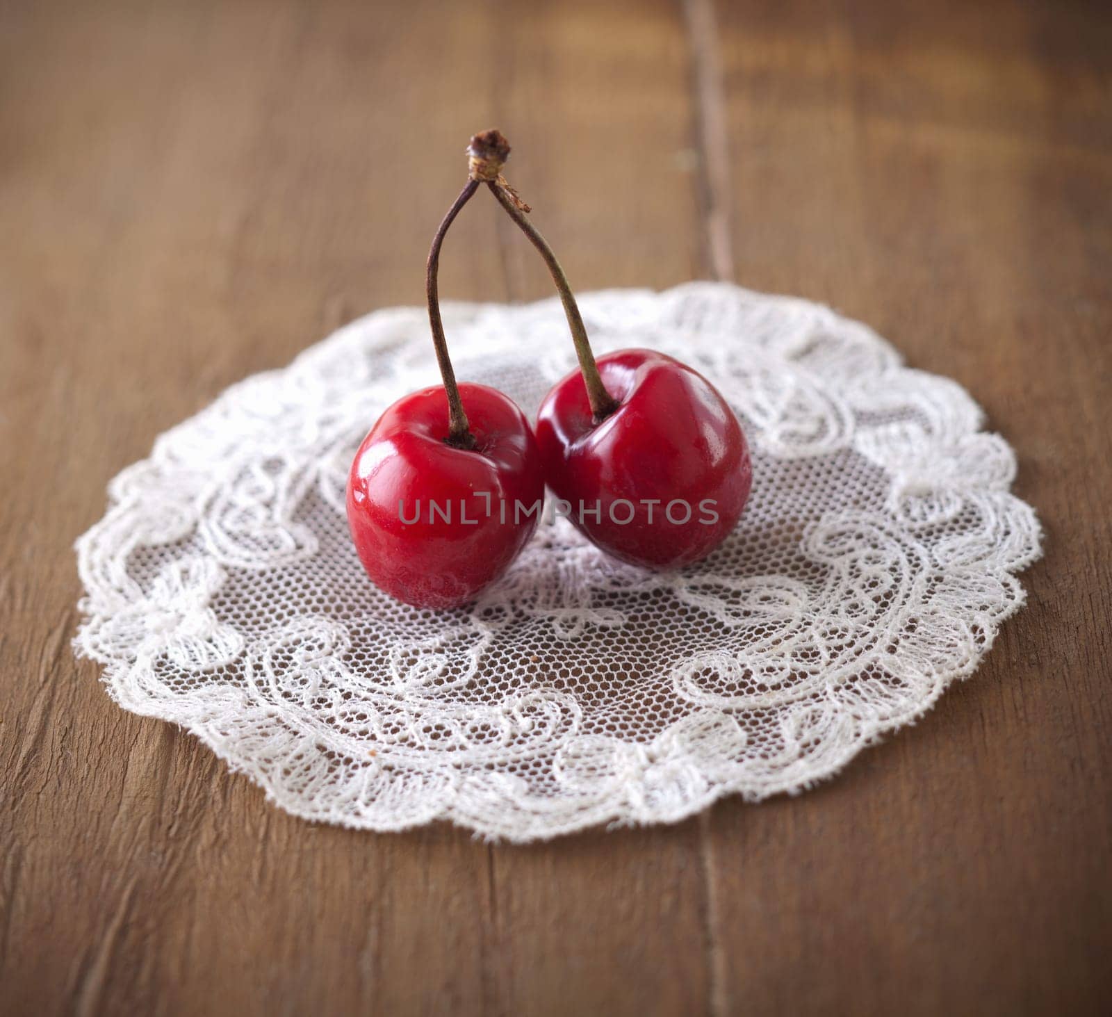 Closeup of two delicious ripe red sweet cherries joined by a common stalk on a lacy doily