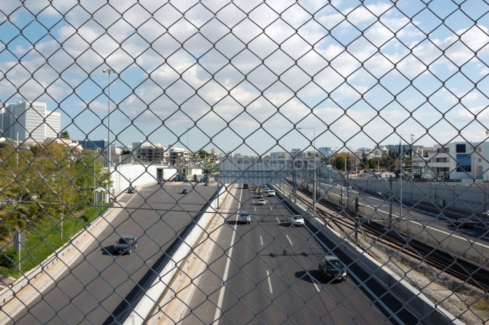 Cars on the motorway and chain link fence. City traffic.