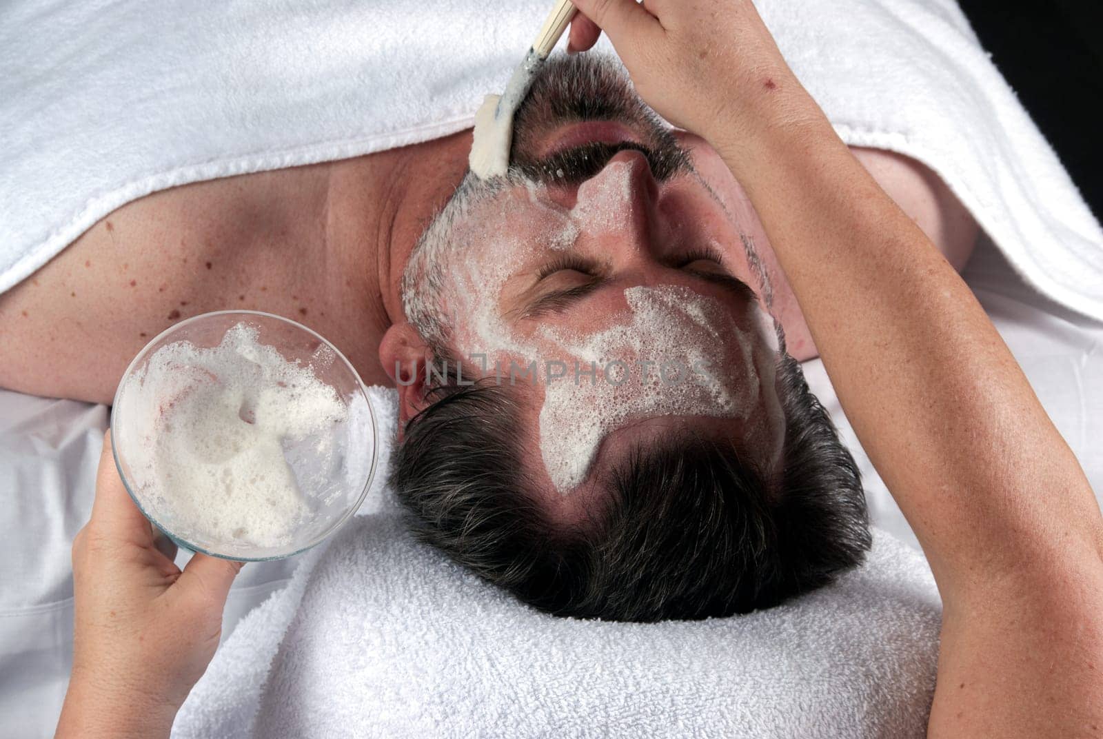 Hand of beautician applying cream to forehead of mature man having a facial.