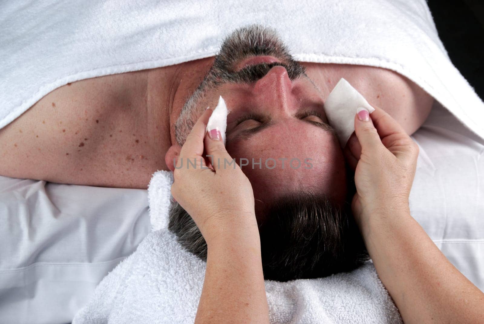 Hand of beautician applying cream to forehead of mature man having a facial.