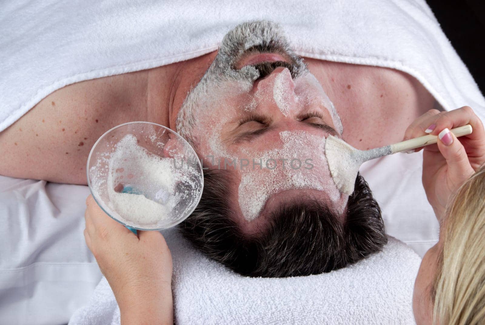 Hand of beautician applying cream to forehead of mature man having a facial.
