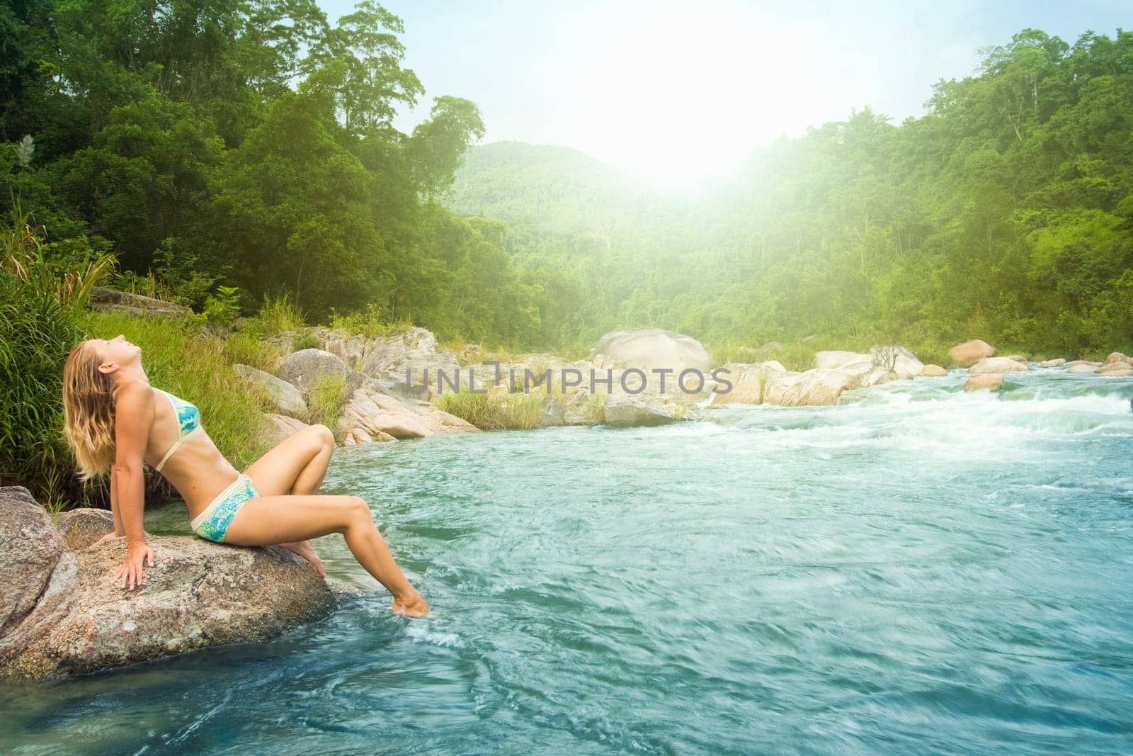 Young woman posing on the stone near jungle river