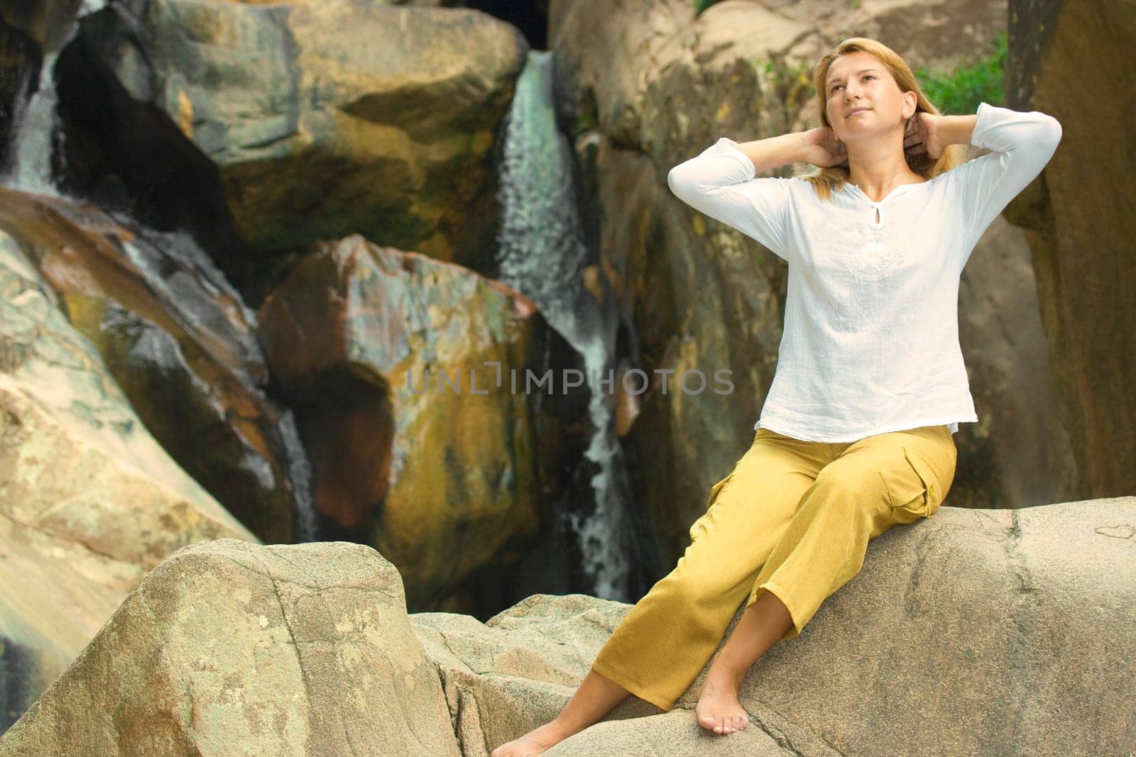 Young woman relaxing on the stone over waterfall background