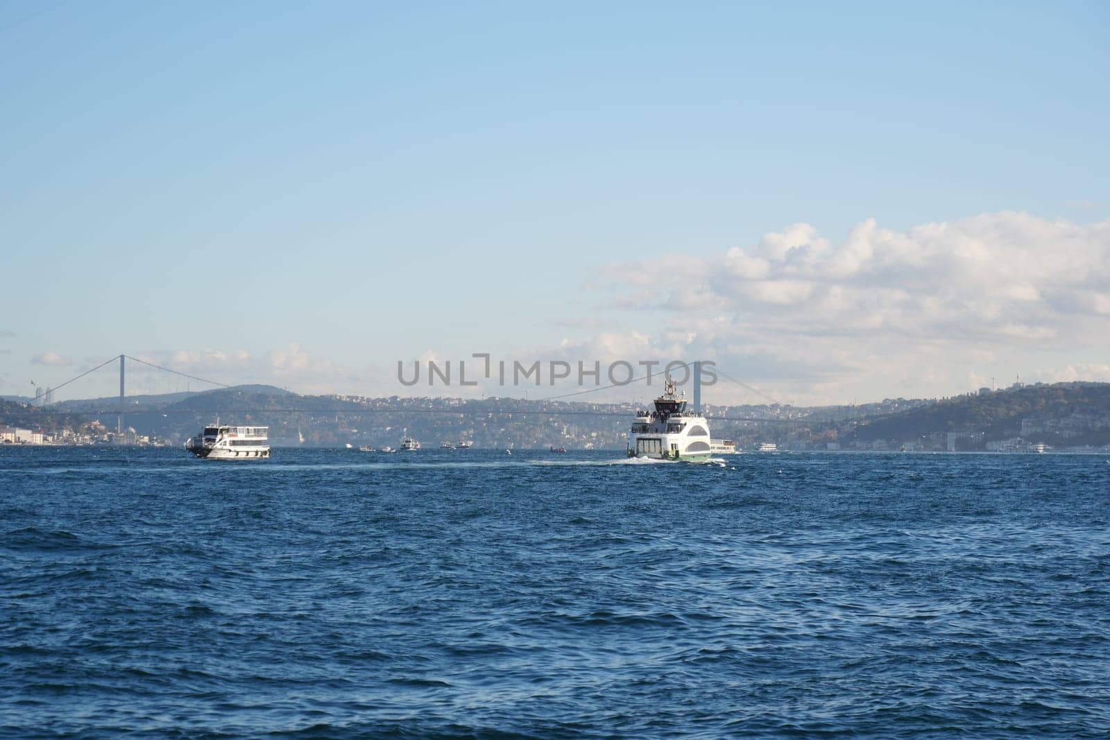 Two boats travel across the blue waters near Istanbul with a bridge in view.