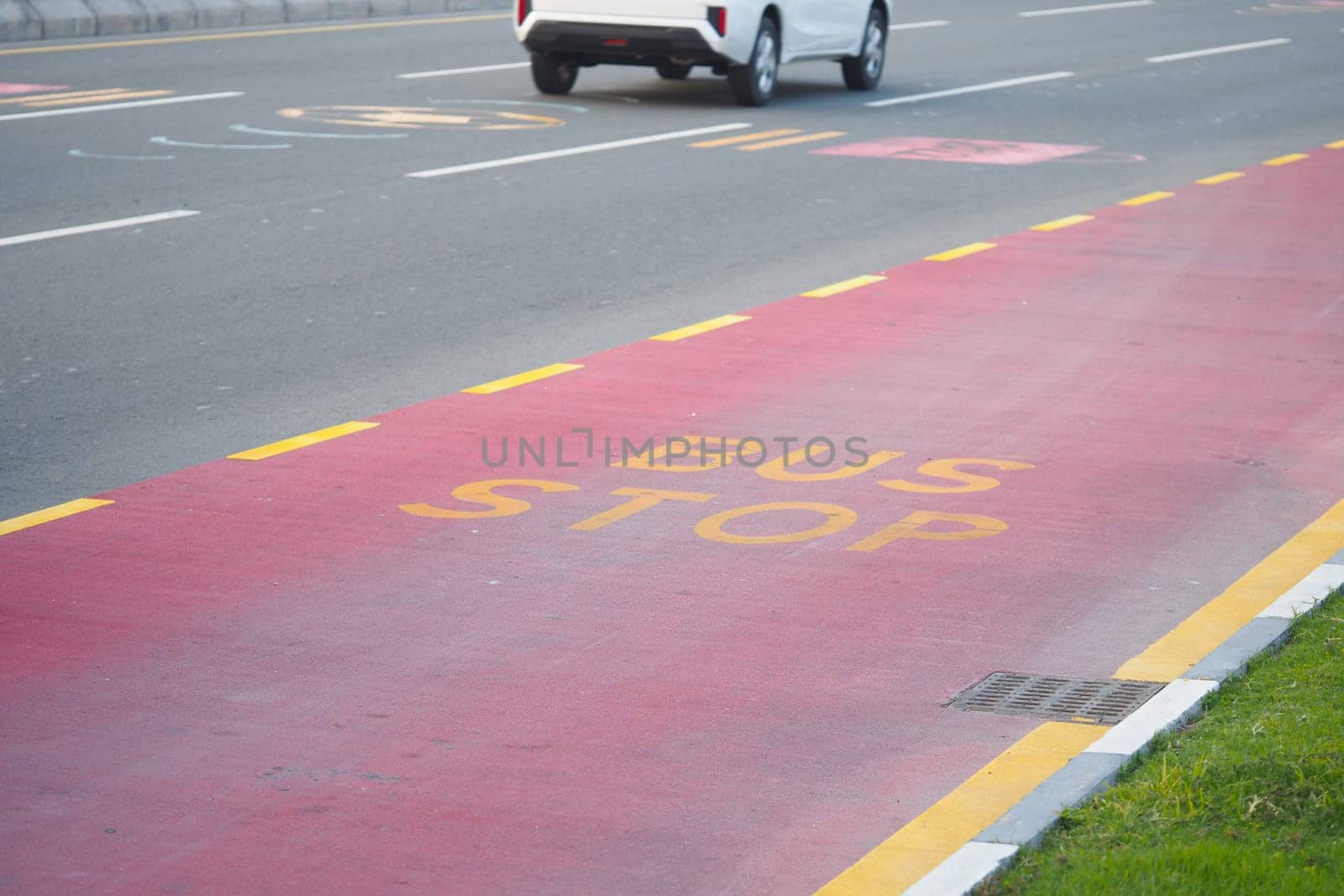 A bus stop is marked on a red lane along a busy road in daylight.